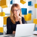 Eine Mitarbeiterin sitzt vor dem Laptop. Im Hintergrund gelbe und blaue Blöcke einer Blockchain